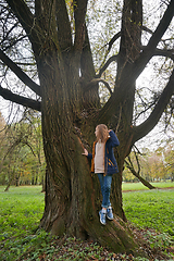 Image showing Dreamily schoolgirl in park near giant willow tree in early autumn