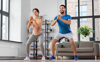 Image showing happy couple exercising and doing squats at home