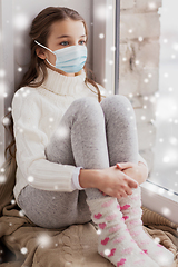 Image showing sad girl in medical mask sitting on sill at home