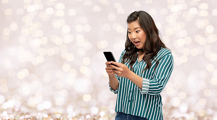 Image showing surprised asian woman using smartphone over lights