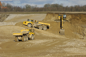 Image showing Yellow dump trucks and excavator are working in gravel pit