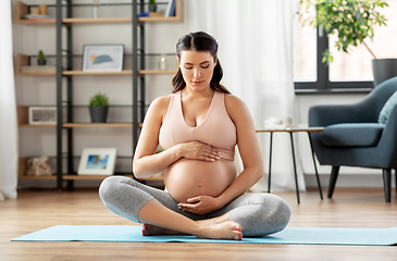 Image showing happy pregnant woman sitting on yoga mat at home