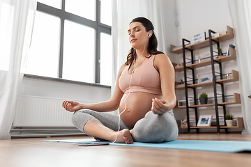 Image showing pregnant woman with earphones doing yoga at home