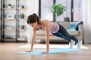 Image showing young woman doing plank exercise on mat at home