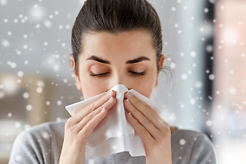 Image showing sick woman blowing nose in paper tissue at home