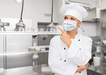 Image showing female chef in mask pointing finger up at kitchen