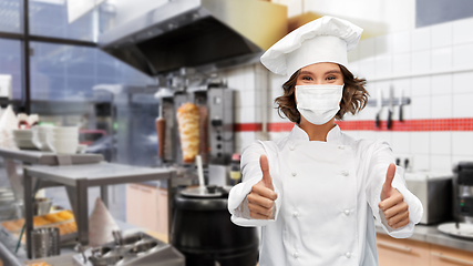 Image showing female chef in mask showing thumbs up at kitchen