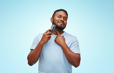 Image showing smiling african man shaving beard with trimmer