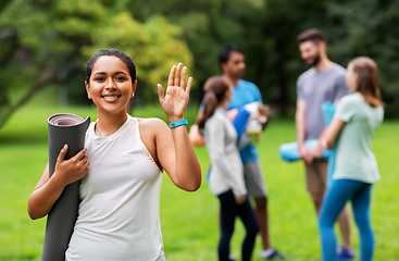 Image showing smiling woman with yoga mat waving hand at park