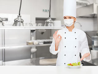 Image showing female chef in mask showing ok sign at kitchen