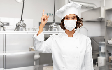 Image showing female chef in mask pointing finger up at kitchen