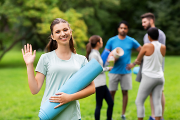 Image showing smiling woman with yoga mat waving hand at park