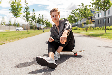 Image showing teenage boy sitting on skateboard on city street