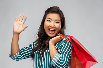 Image showing happy asian woman with shopping bags waving hand