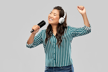 Image showing asian woman in headphones with hairbrush singing