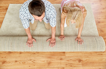 Image showing happy couple unrolling carpet or rug at home