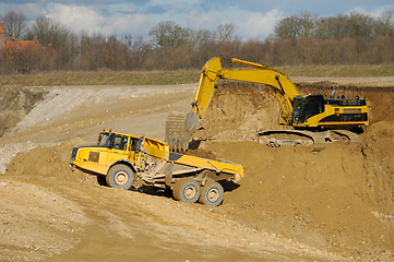 Image showing Yellow dump trucks and excavator are working in gravel pit