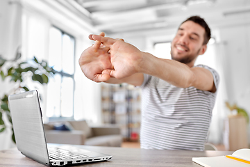 Image showing happy man with laptop stretching at home office