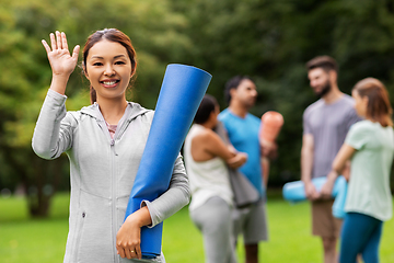 Image showing smiling woman with yoga mat waving hand at park