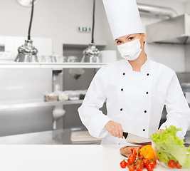 Image showing female chef in mask cutting vegetables at kitchen