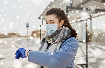 Image showing woman in mask looking at wristwatch at bus stop