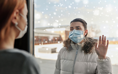 Image showing woman in mask looking to friend through window