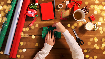 Image showing hands wrapping christmas gift into paper at home