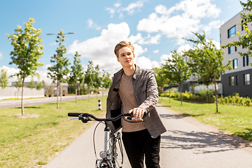 Image showing young man with bicycle walking along city street