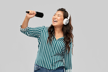 Image showing asian woman in headphones with hairbrush singing