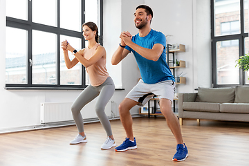 Image showing happy couple exercising and doing squats at home
