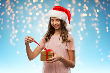 Image showing teenage girl in santa hat opening christmas gift