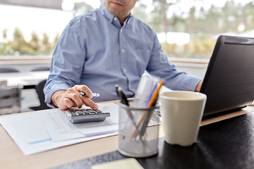 Image showing man with calculator and papers working at home