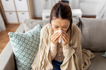 Image showing sick woman blowing nose in paper tissue at home