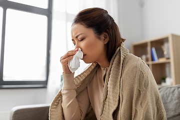 Image showing sick woman blowing nose in paper tissue at home