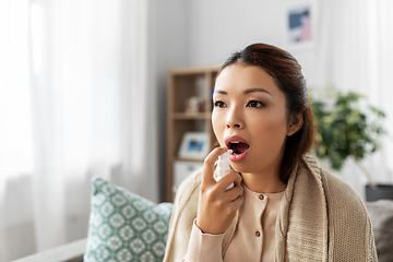 Image showing sick asian woman using oral spray medicine at home