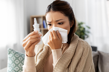 Image showing sick asian woman with nasal spray blowing nose