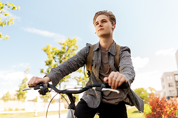 Image showing teenage boy with earphones and bag riding bicycle