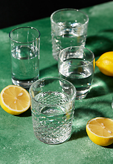 Image showing glasses with water and lemons on green background