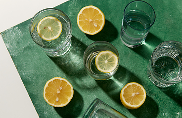 Image showing glasses with water and lemons on green background