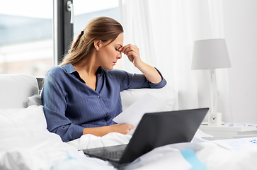 Image showing young woman with laptop and papers in bed at home