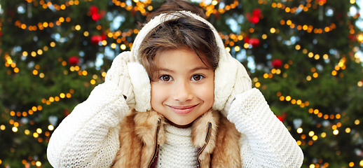 Image showing happy little girl in earmuffs over christmas trees