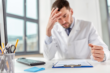 Image showing stressed male doctor with clipboard at hospital