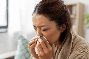 Image showing sick woman blowing nose in paper tissue at home