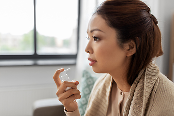 Image showing sick asian woman using oral spray medicine at home