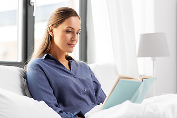 Image showing young woman reading book in bed at home