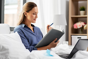 Image showing young woman with laptop and papers in bed at home