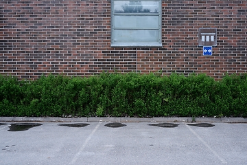 Image showing empty parking near red brick wall and green bushes, deadpan phot