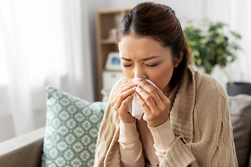 Image showing sick woman blowing nose in paper tissue at home