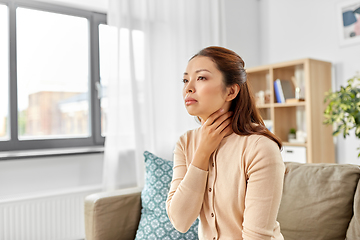 Image showing sick asian woman touching her sore throat at home