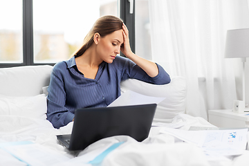 Image showing young woman with laptop and papers in bed at home